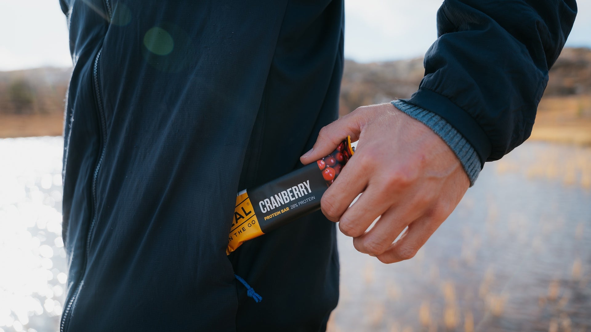 Person holding a cranberry protein bar with a blurred natural background